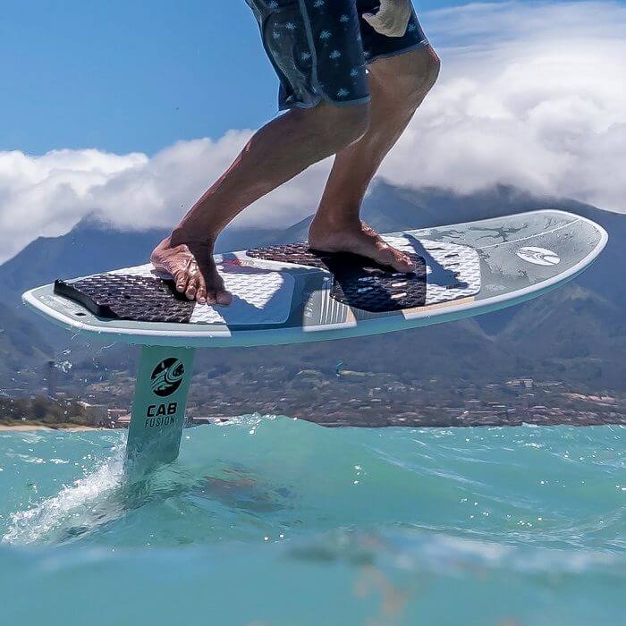 Surfer auf einem Foilboard surft über die Wellen unter einem klaren blauen Himmel.