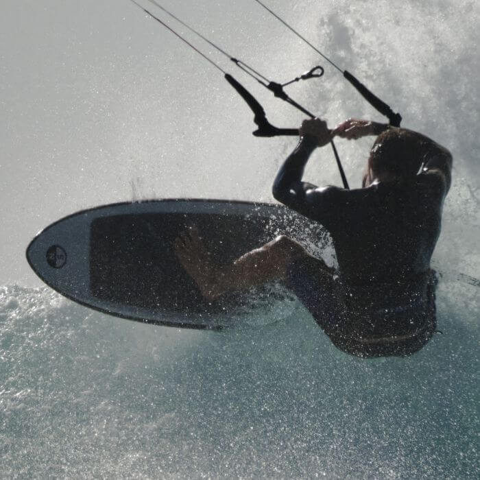 Surfer springt auf seinem Kiteboard durch die Wellen im Sonnenlicht, mit Wasserspritzern um ihn herum.