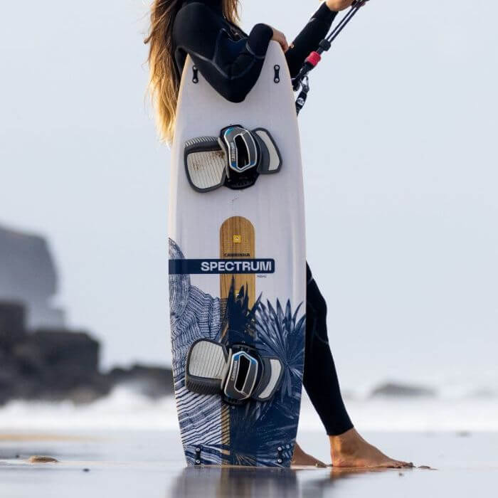 Surferin mit einem Spectrum-Surfbrett am Strand, bereit zum Kitesurfen in den Wellen.