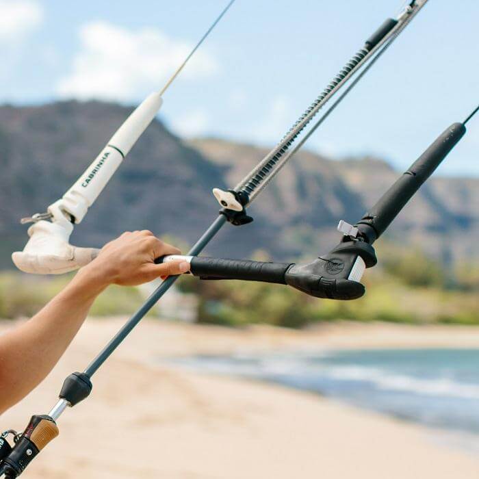 Hände halten eine Kitebar am Strand mit Blick auf das Meer und Hügel im Hintergrund