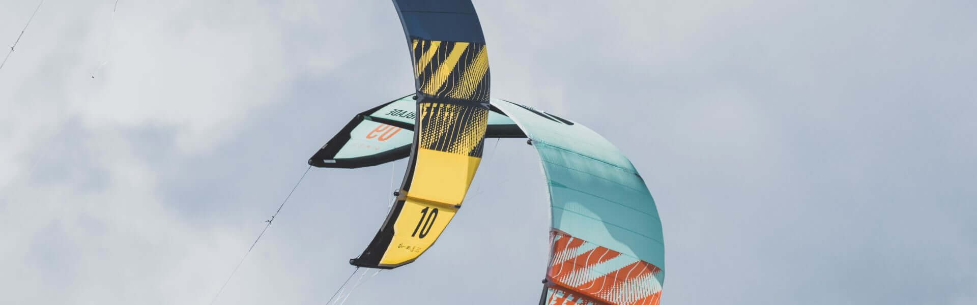Bunte Kitesurf-Tücher am Himmel, die in der Luft schwingen und eine dynamische Sportatmosphäre schaffen.