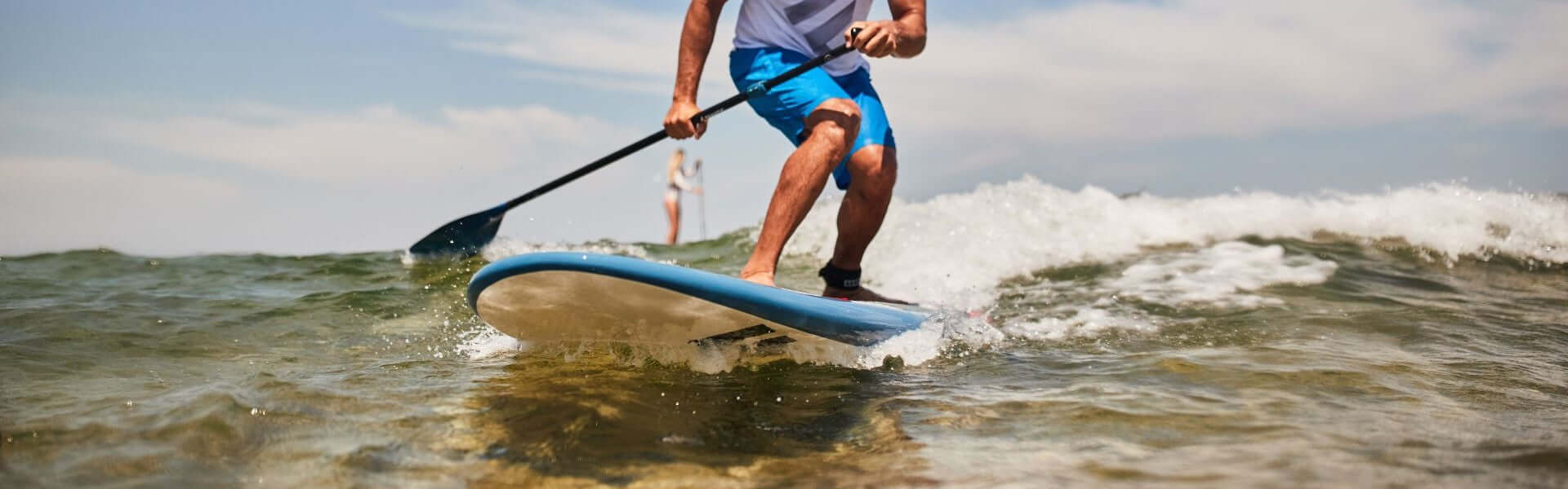 Surfender Mann auf einem Stand-Up-Paddle-Board, der Wellen reitet und Spaß im Wasser hat.