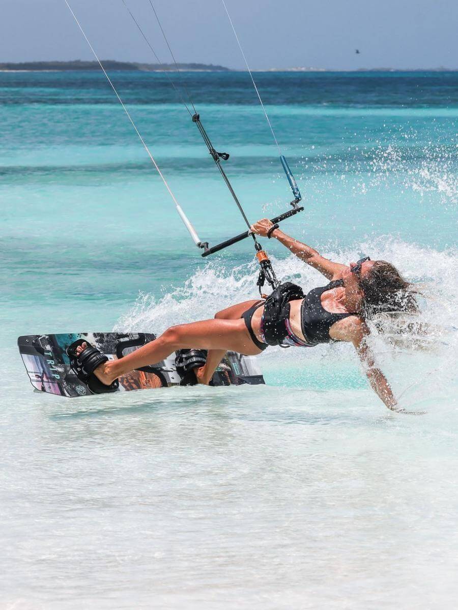 Kitesurferin auf türkisblauem Wasser, genießt das Adrenalin im Wasserport, ideal für unseren Online Surfshop.