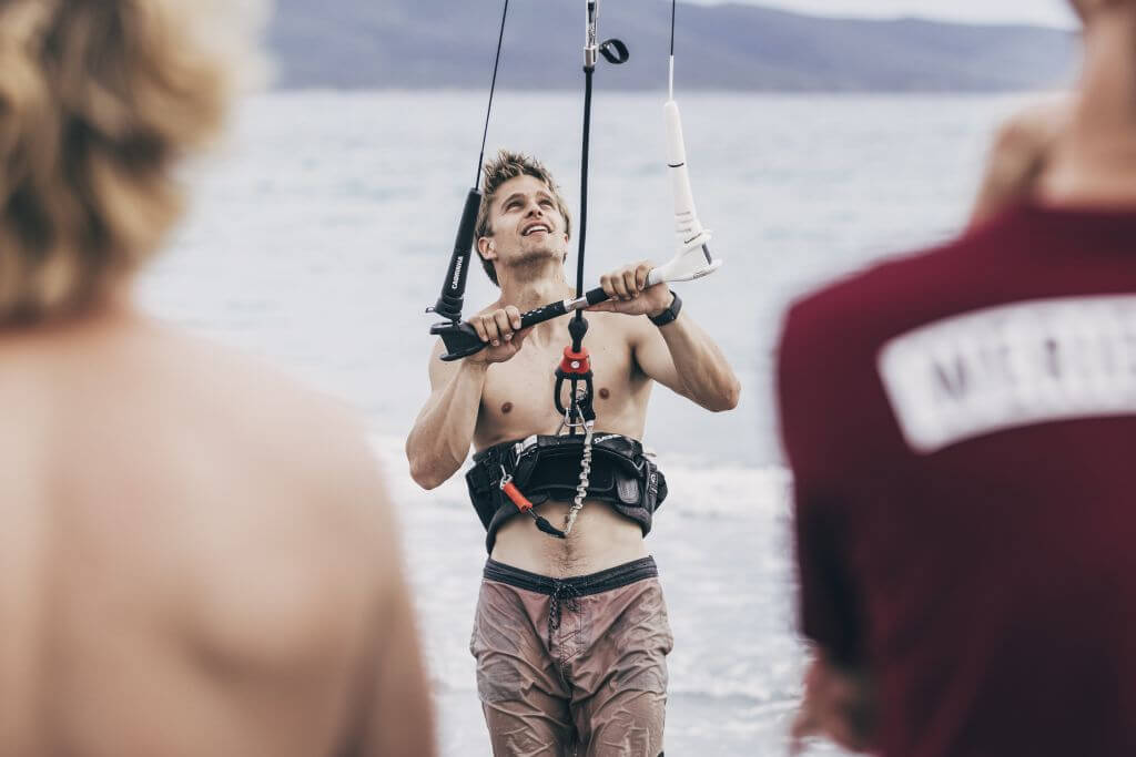 Kiteboarder am Strand, konzentriert beim Kitesurfen, mit Kite vor Wasserlandschaft.