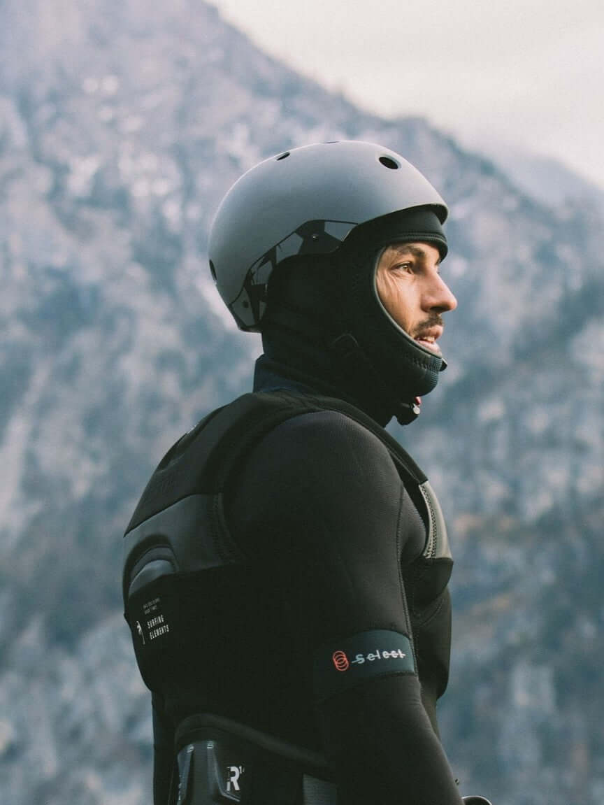 Mann mit Helm und Neoprenanzug, der in die Ferne sieht, vor felsiger Berglandschaft.