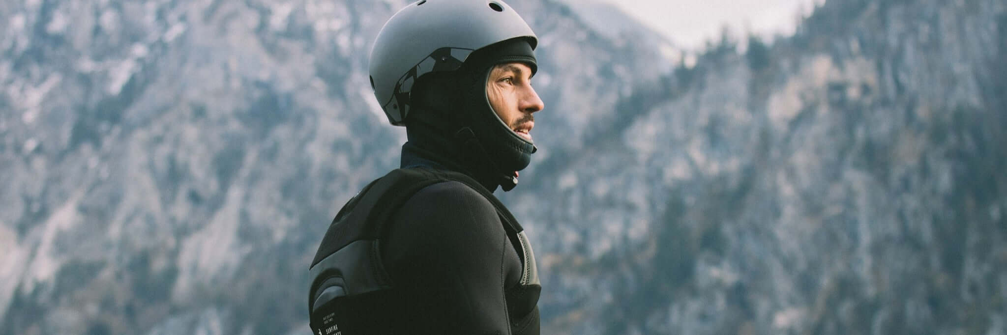 Sportler mit Helm und Neoprenanzug, bereit für Abenteuer in einer majestätischen Berglandschaft.