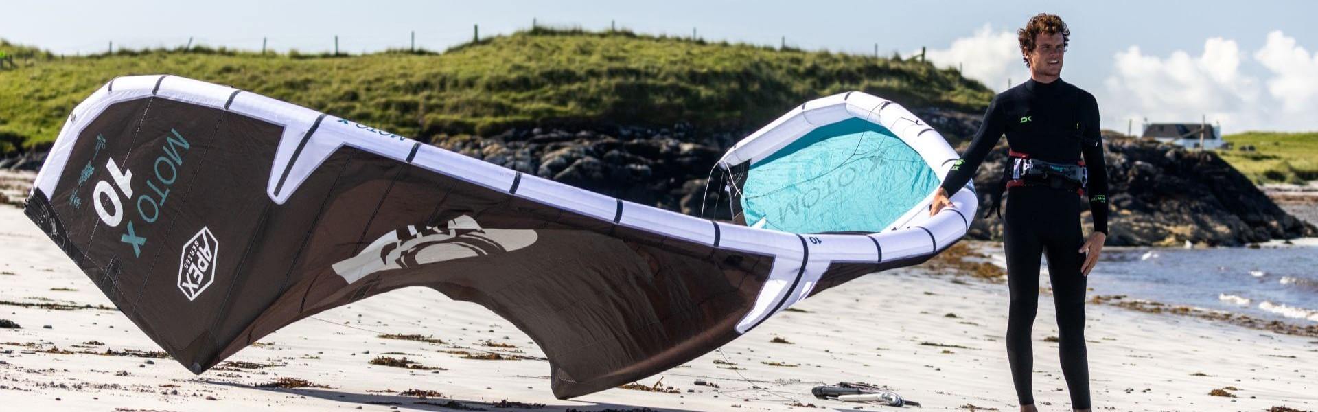 Kitesurfer am Strand mit einem schwarzen und blauen Kite, ideal für Wassersport im Surfshop.