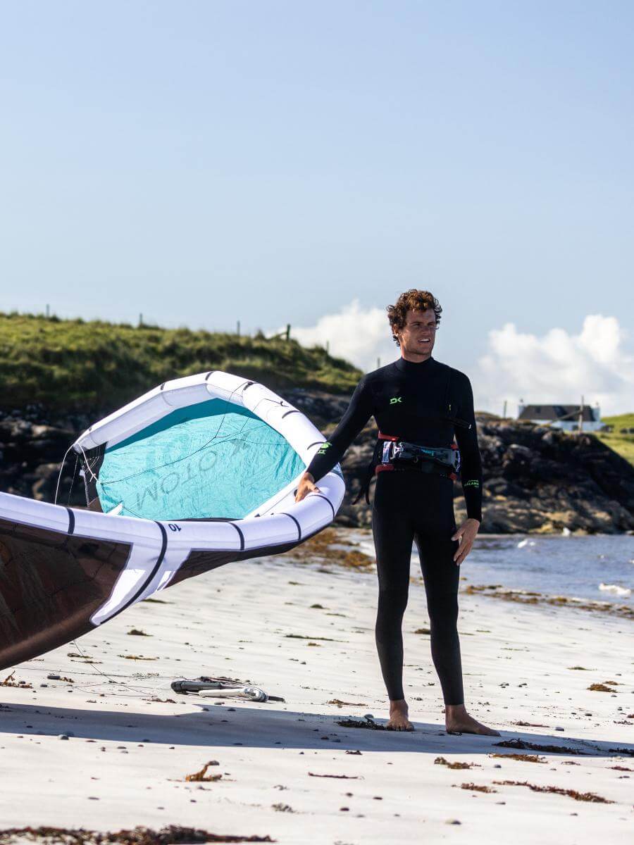 Surfer in Neoprenanzug mit Windsurfbrett am Strand, bereit für das Abenteuer im Wasser.