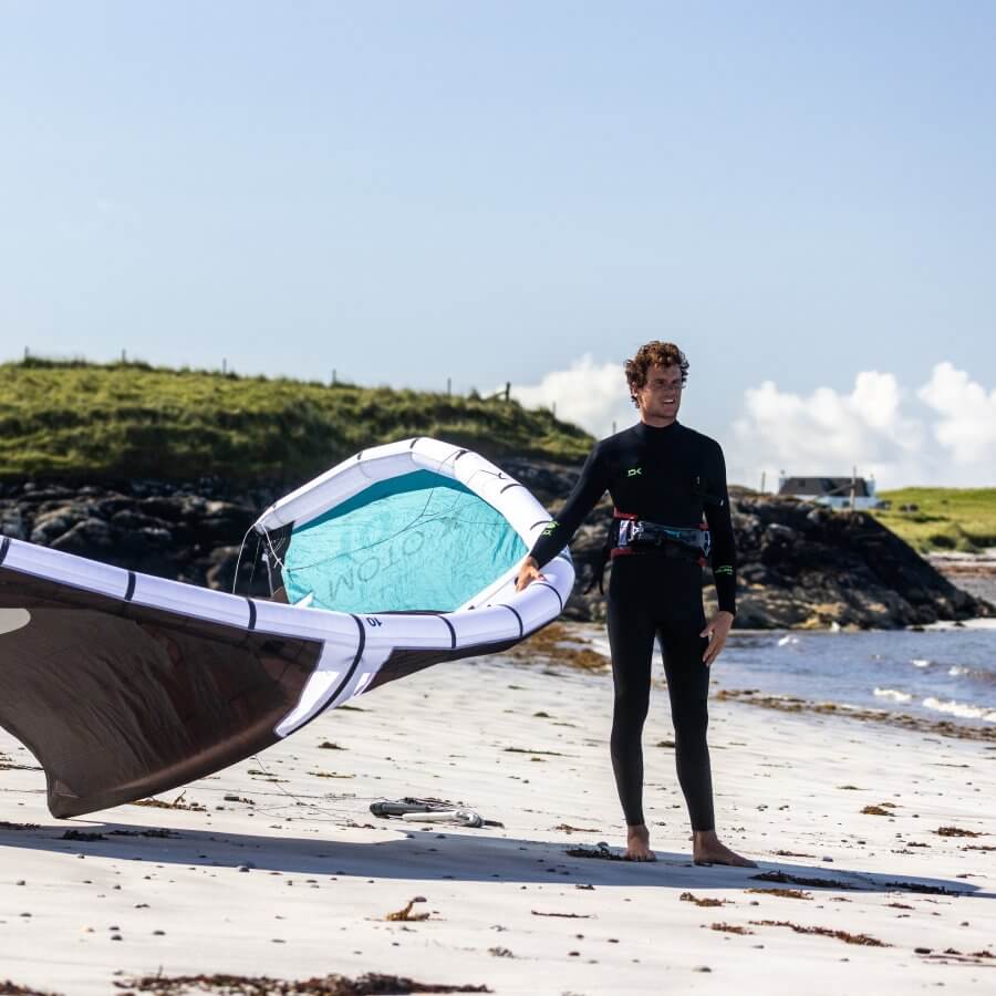 Surfer in Neoprenanzug mit Windsurfbrett am Strand, bereit für das Abenteuer im Wasser.
