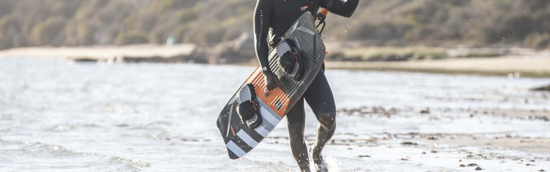 Kitesurfer trägt ein Board am Strand, bereit für sportliche Aktivitäten im Wasser.
