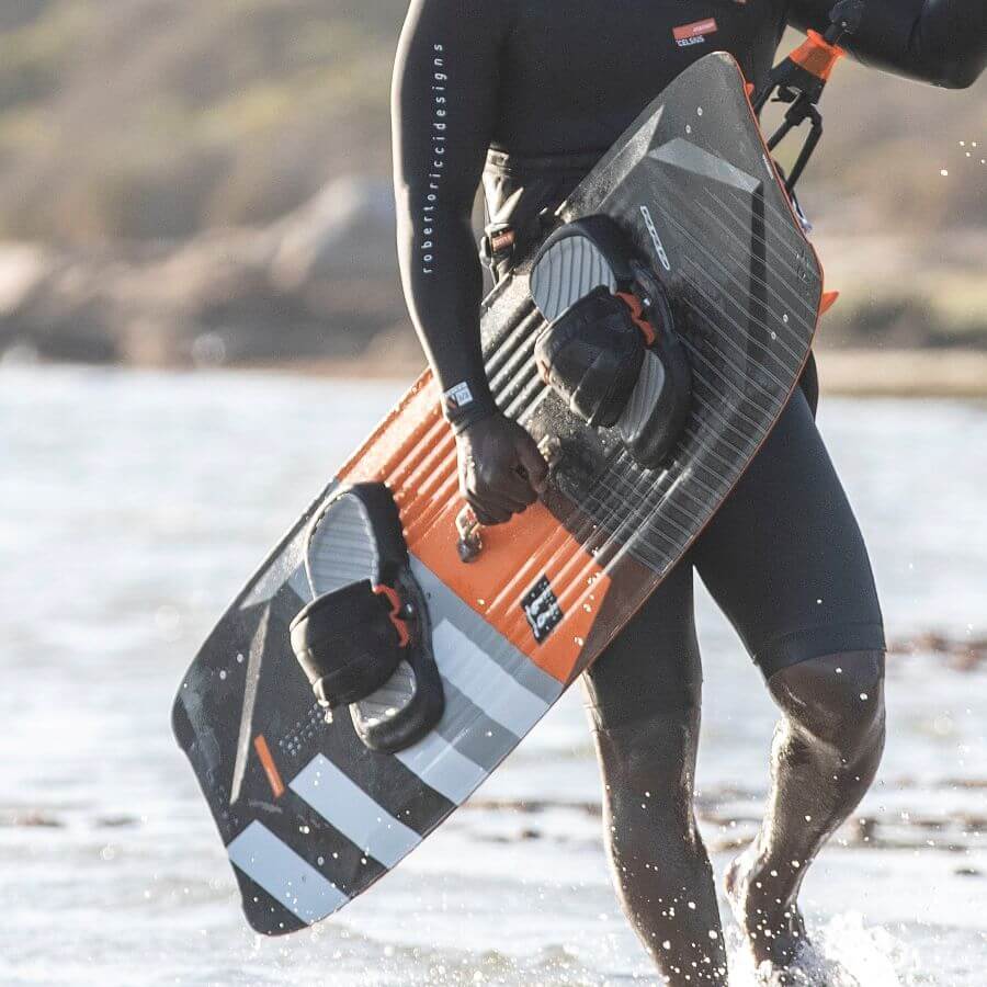 Surfer mit einem Kiteboard am Strand, bereit zum Kitesurfen in der Sonne.