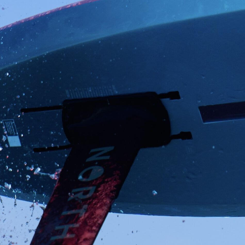 Unterwasseransicht eines Surfbretts mit der Aufschrift 'NORTH', umgeben von spritzendem Wasser.