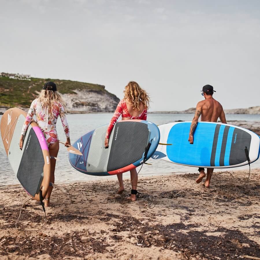 Drei Surfer mit Paddleboards am Strand, bereit zum Paddeln, genießen einen sonnigen Tag am Meer.