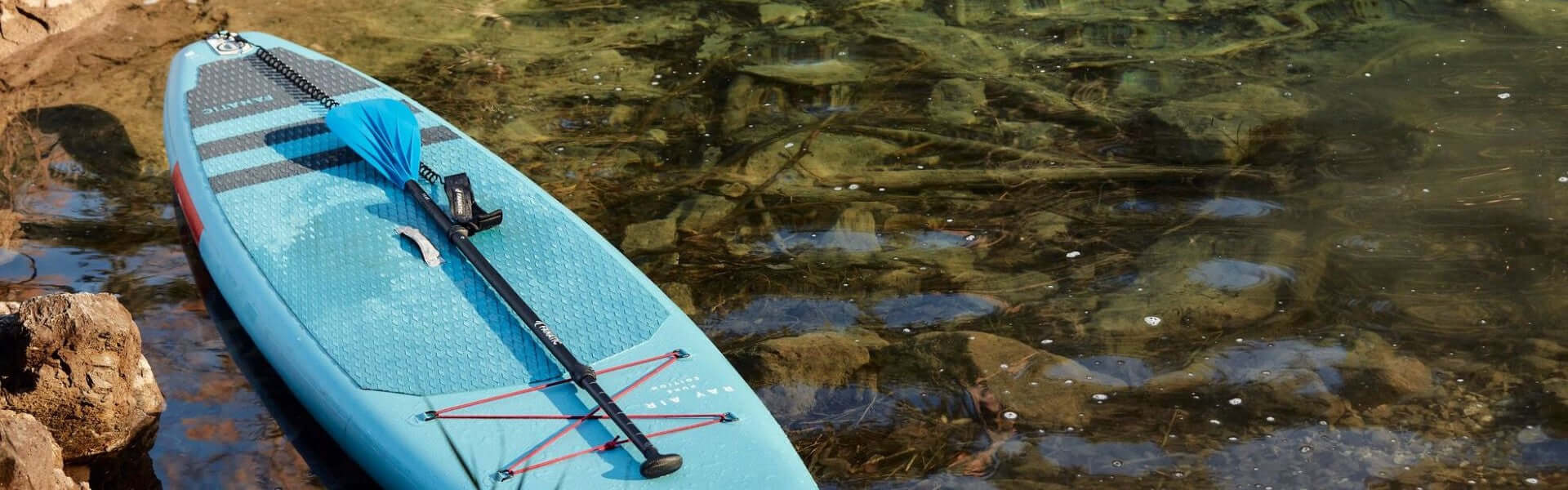 Blaue Stand-Up-Paddle-Board am Ufer mit Paddel und klarer Wasseroberfläche.