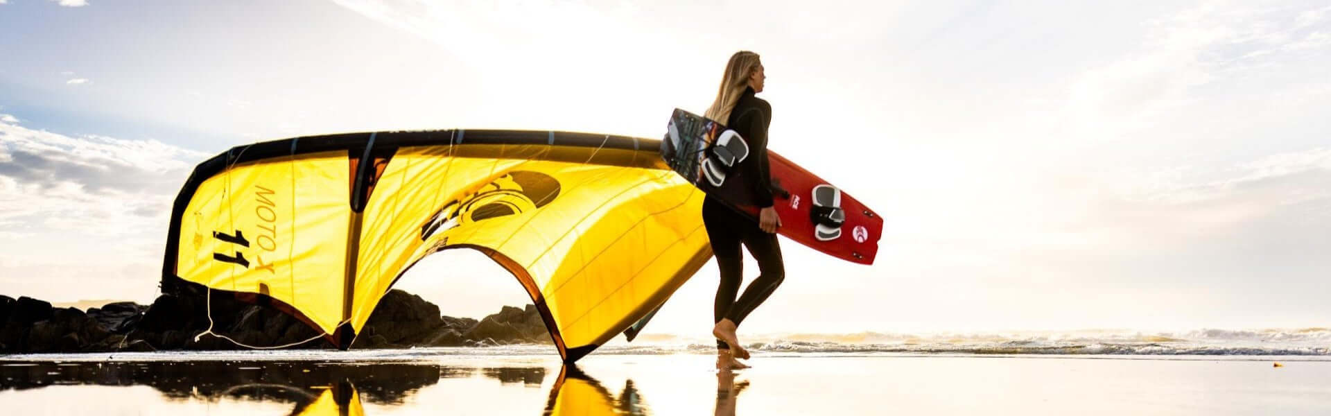 Kitesurferin mit gelbem Kite und Board am Strand im Sonnenuntergang, bereit zum Wassersport.