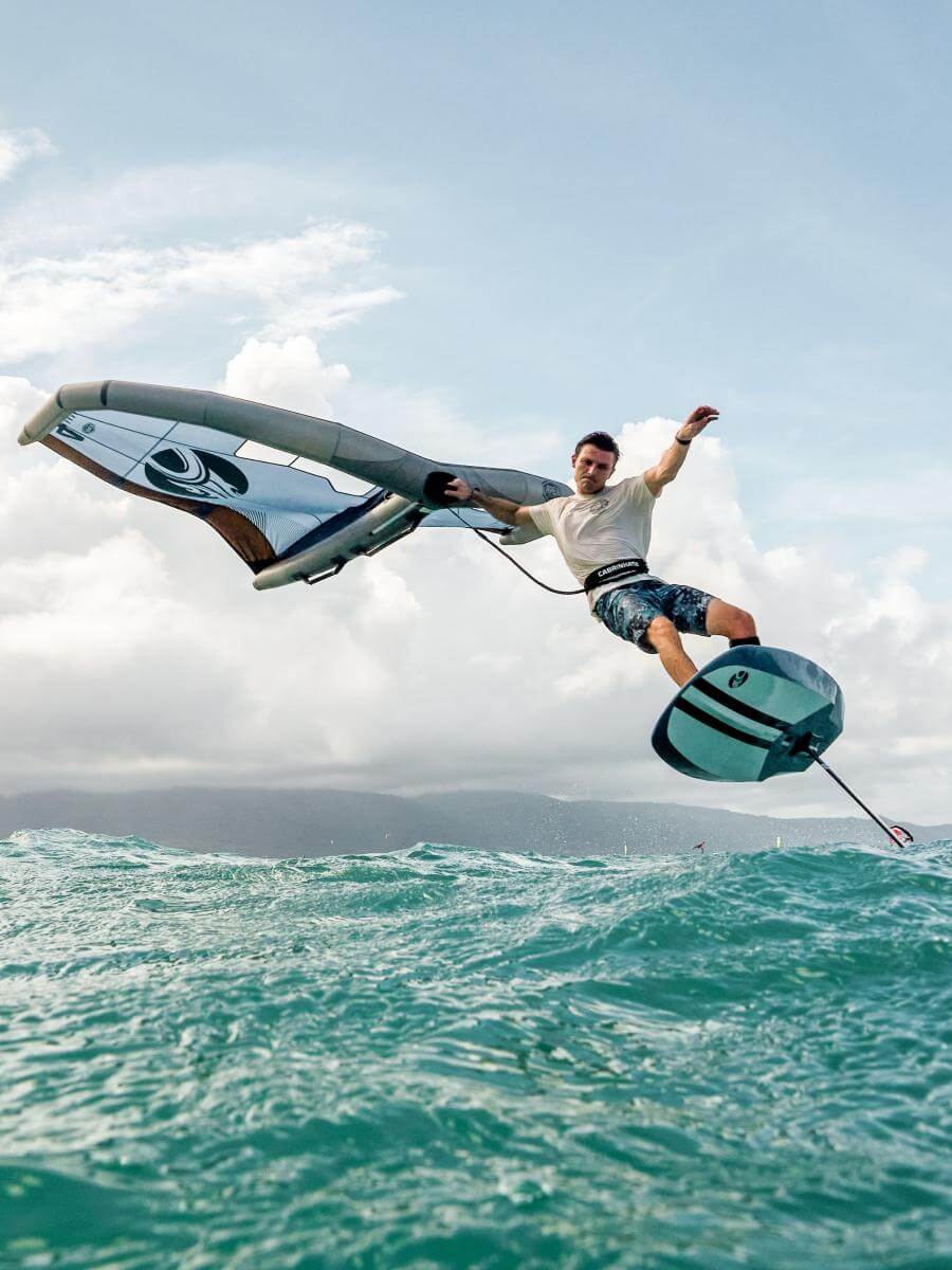 Mann beim Foil-Wing-Surfen auf den Wellen, mit Himmel und Wolken im Hintergrund.